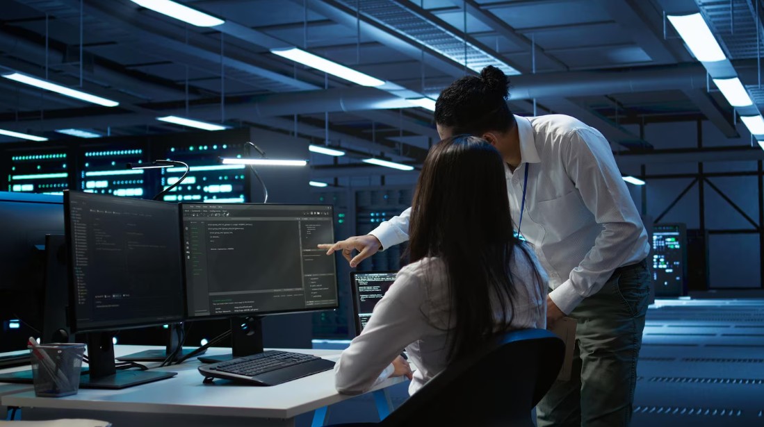 Two professionals focus on computer screens in a dark room, showcasing Managed IT Services For Small Businesses in Asheville, NC.